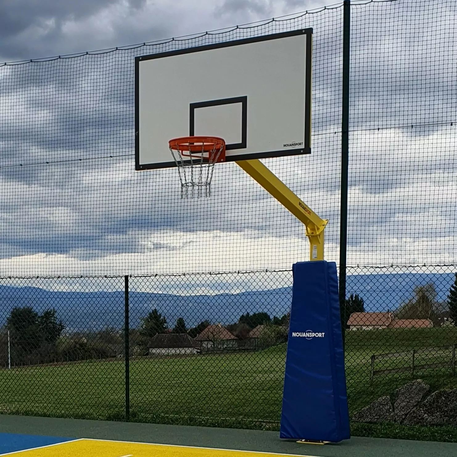 Cette image est une photographie d'un but de basket extérieur comprenant un bâti, un panneau, un cercle et un filet en chaine. Elle illustre l'ensemble des équipements sportifs de basket extérieur que Nathis peut fournir et installer pour les collectivités de Bretagne.