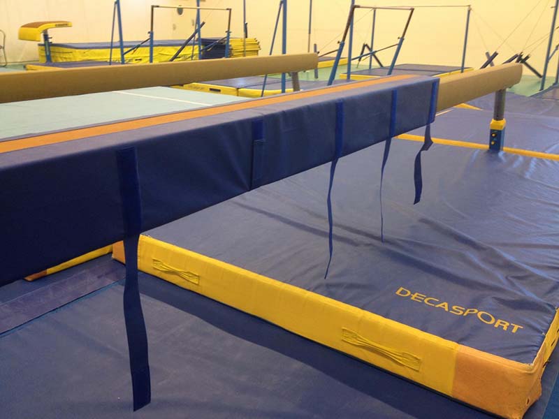 Cette image est une photographie d'une salle de gymnastique. Elle met en évidence les agrès, protections et autres équipements sportifs de gymnastique que Nathis peut fournir et installer aux collectivités de Bretagne.