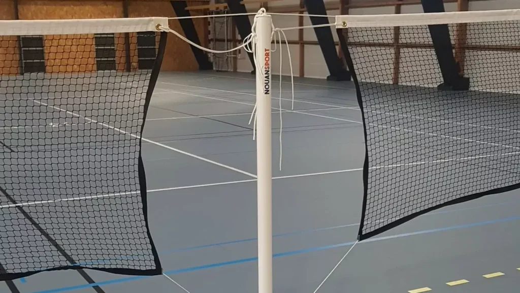 Cette image est une photographie d'un poteau de volley et de filets de volley. Elle illustre les équipements sportifs de volley que Nathis peut fournir et installer aux collectivités de Bretagne.