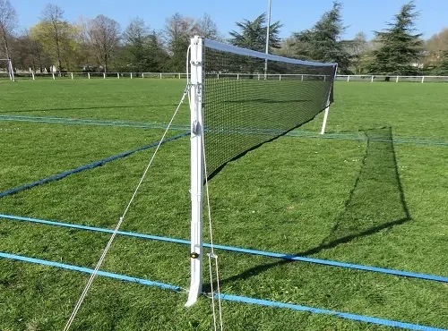 Cette image est une photographie d'un terrain de Air Badminton comprenant le filet, les poteaux et le tracé. L'image illustre les équipements sportifs de badminton intérieur et extérieur que Nathis peut fournir et installer aux collectivités de Bretagne.