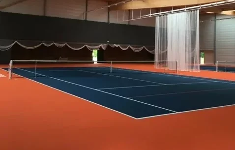 Cette image est une photographie d'un terrain de tennis intérieur. Elle illustre l'ensemble des équipements sportifs de tennis que Nathis peut fournir et installer pour les collectivités de Bretagne.